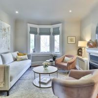 Elegant living room with automated shades in bay window, fireplace, mirror, and blush accent chairs.