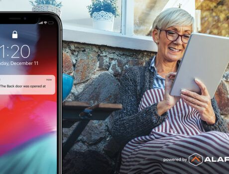 woman looking at ipad while outdoors. Phone interface showing an Alarm.com smart alert.