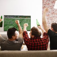 Three people sitting on a couch watching a football game and cheering on their team.