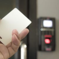 A hand holding a key card with an access control system displayed in the background.