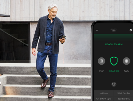 Man using a smartphone to control his home security system while walking down stone steps.