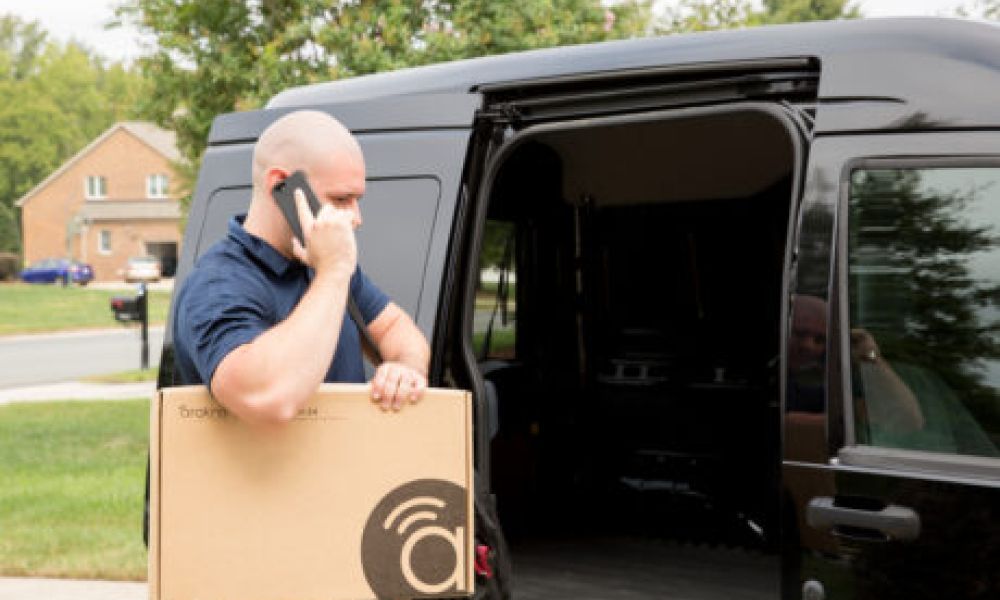 <span class="uk-h4">person talking on phone next to a work van while holding an Araknis product box</span>