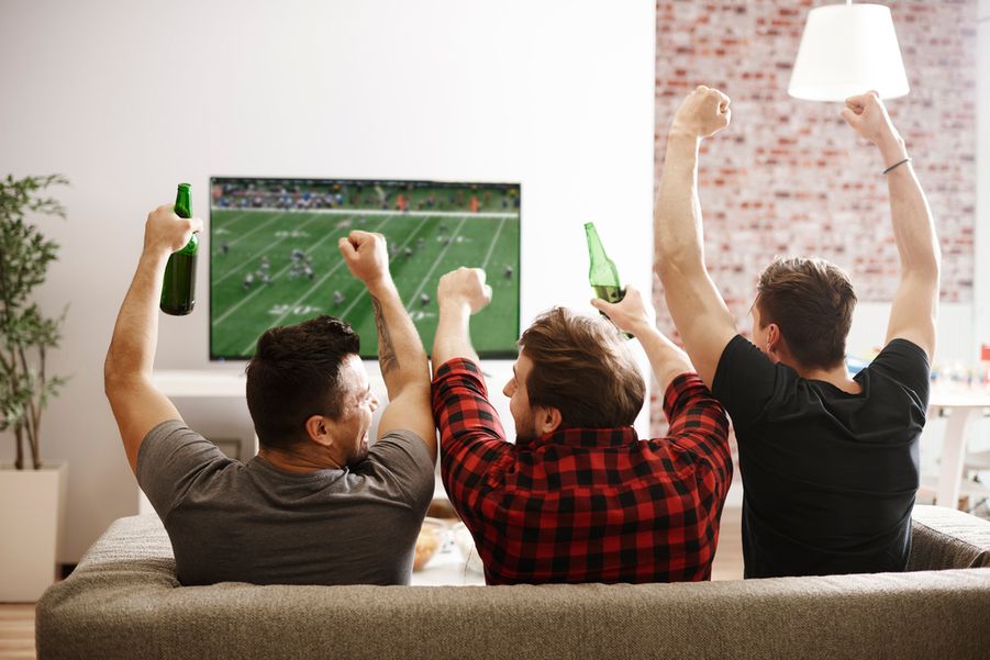 Three people sitting on a couch watching a football game and cheering on their team.