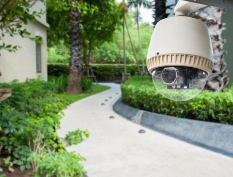 A driveway in the background with a home security camera in the foreground.