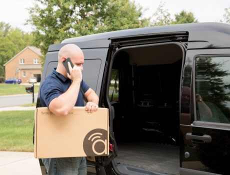 person talking on phone next to a work van while holding an Araknis product box