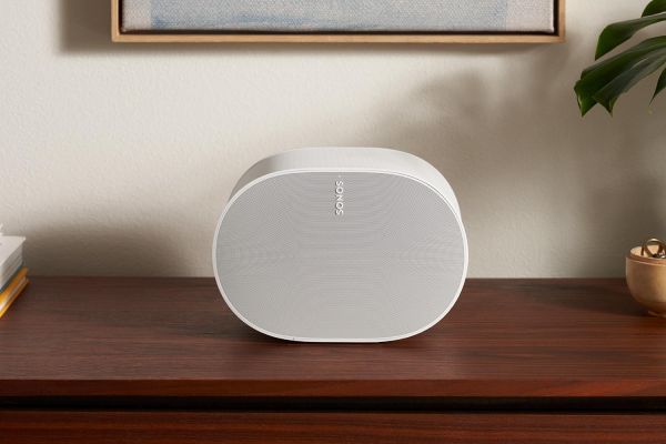 A sleek, white speaker resting on a wooden surface in a minimalist room, with abstract art hanging on the wall behind.