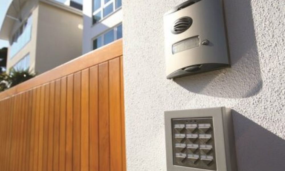 <span class="uk-h4">An exterior of a home with a smart home alarm and keypad on the wall in focus.</span>