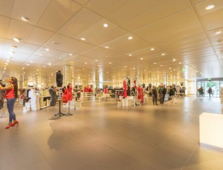 Shoppers in a well-lit retail space, shopping through clothes racks