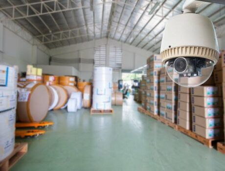 A surveillance camera in focus with a warehouse in the background.