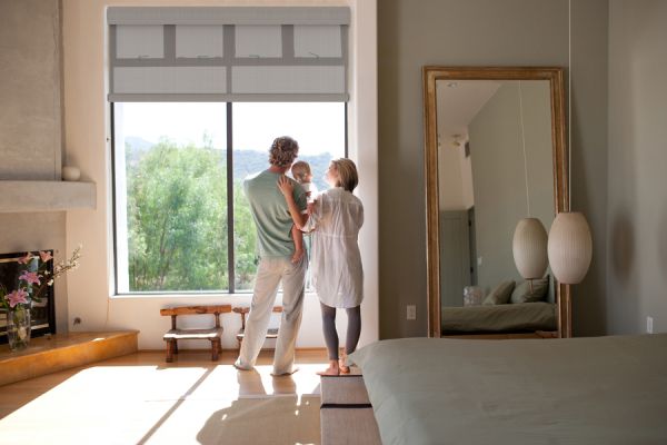 A young couple stands with their baby looking out a large picture window.