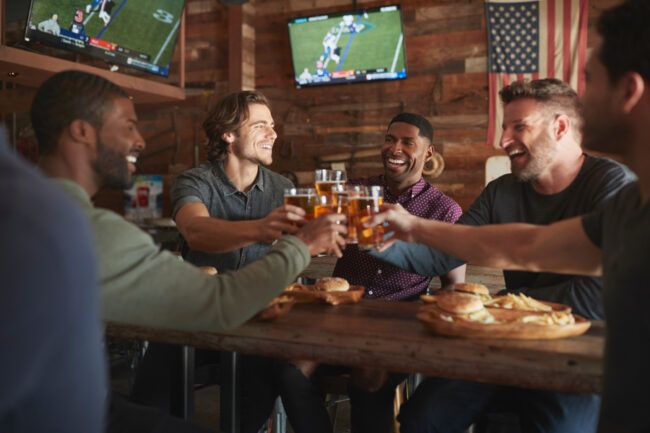 Group of friends drinking beer at a sports bar with multiple screens.