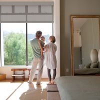 A young couple stands with their baby looking out a large picture window.